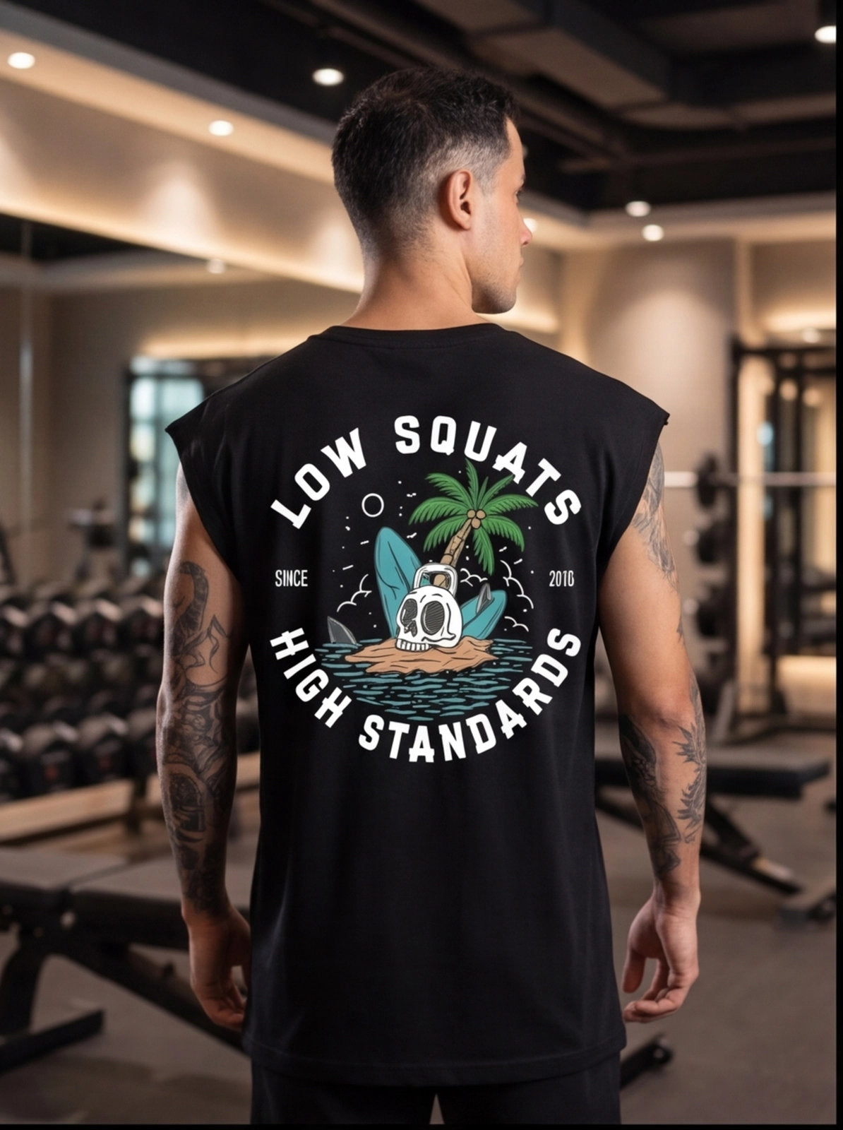 Man wearing black gym tank with 'Low Squats High Standards' graphic, skull, palm tree, kettlebell in gym