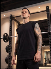 Man in black sleeveless gym shirt with tattoos, standing near squat rack for functional fitness training