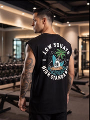 Man in gym wearing black sleeveless fitness shirt with 'Low Squats High Standards' graphic, palm tree, kettlebell design.