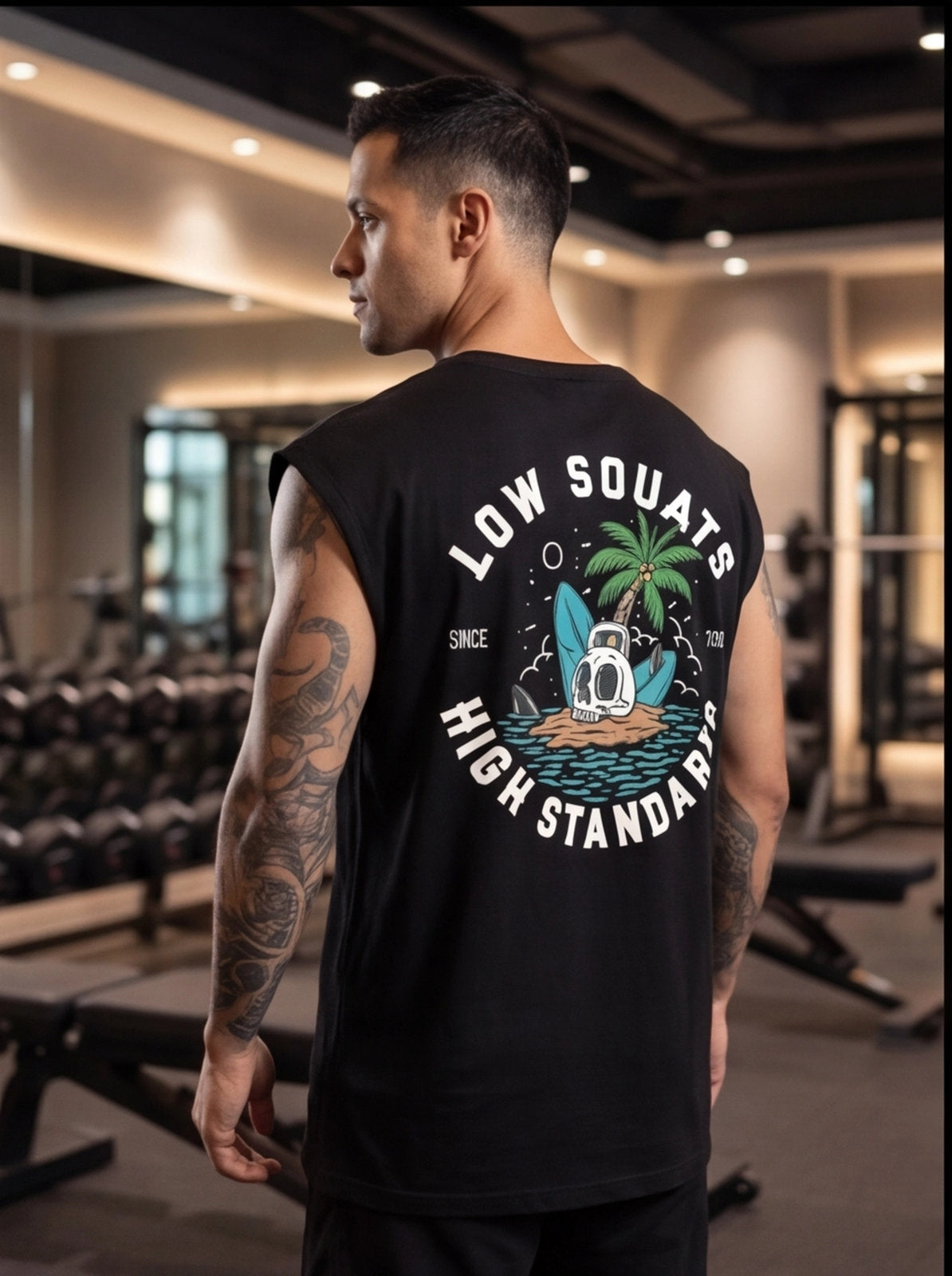Man in gym wearing black sleeveless fitness shirt with 'Low Squats High Standards' graphic, palm tree, kettlebell design.
