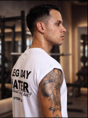 Man in gym wearing white 'Leg Day Hater' workout shirt, tattooed arm, fitness apparel