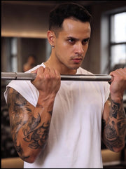 Man lifting barbell in gym, tattooed arms, focused workout for functional fitness performance