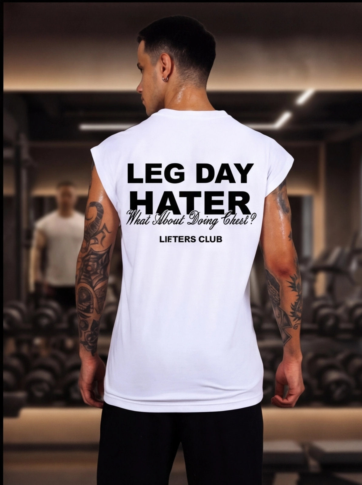 Man wearing white 'Leg Day Hater' gym shirt in fitness studio, tattoos visible, motivational workout apparel