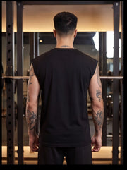 Man wearing black sleeveless gym shirt, showcasing tattoos, standing in front of squat rack