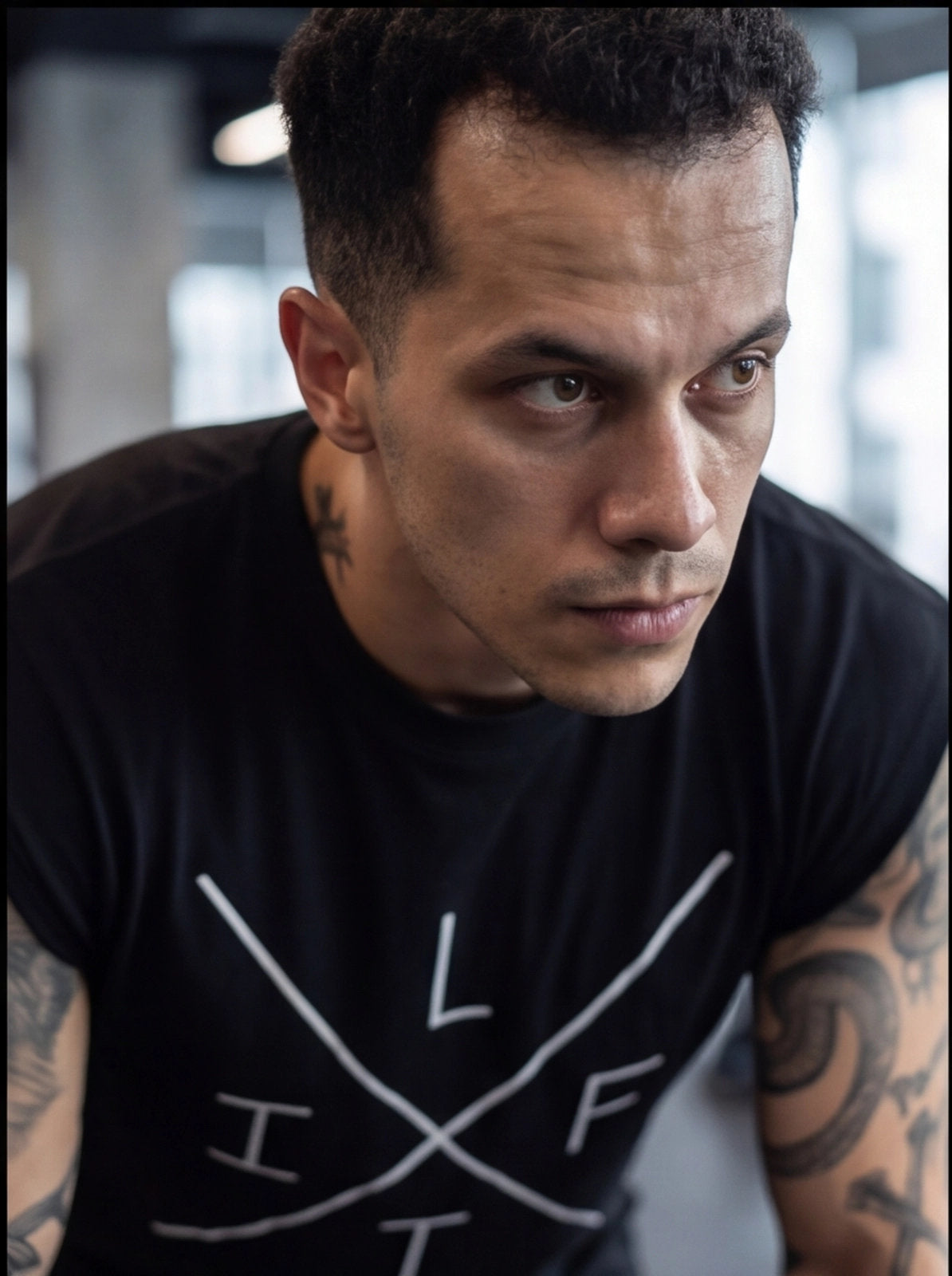 Athlete in black fitness t-shirt with white graphic, focused expression, tattoos visible, gym setting