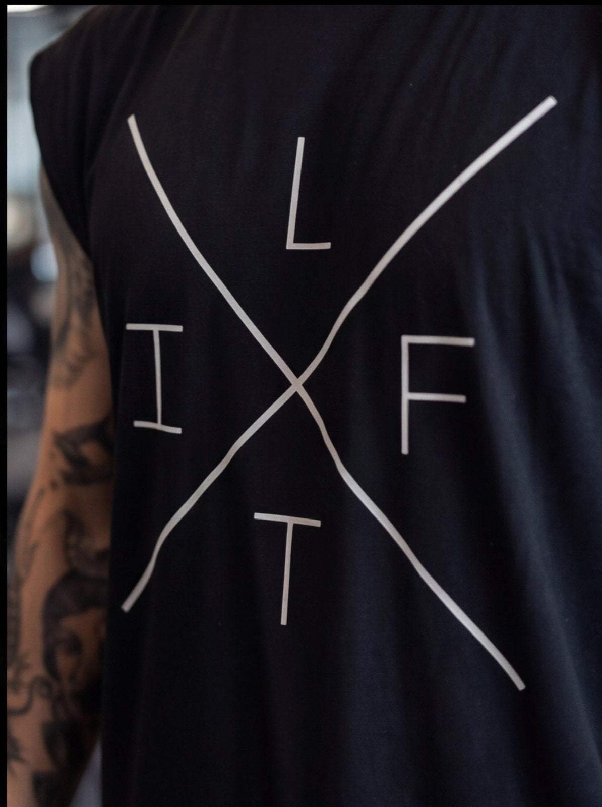 Black sleeveless fitness tank with 'LIFT' graphic design, worn by tattooed athlete for functional training.