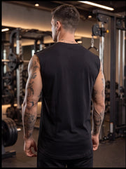 Man in black sleeveless gym shirt with tattoos, standing in fitness center