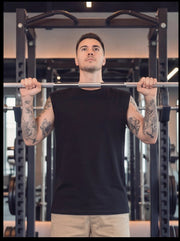 Man lifting barbell in gym, wearing black sleeveless shirt for functional fitness training
