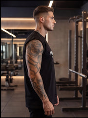 Athlete in black sleeveless gym shirt with tattoos, standing in fitness center for functional training