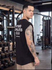 Man in gym wearing black 'Hybrid Athletes Club' sleeveless shirt, showcasing athletic wear for functional fitness training.