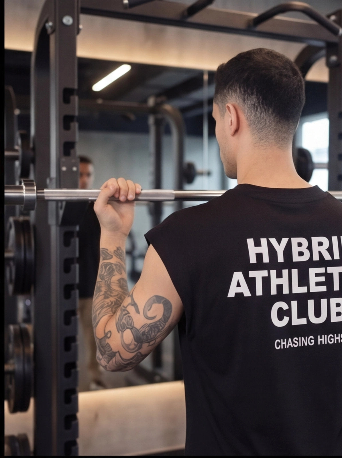 Man lifting barbell in gym wearing Hybrid Athlete Club shirt, showcasing functional fitness gear for athletes.