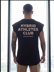 Man wearing black Hybrid Athletes Club sleeveless shirt, standing by window, fitness apparel for athletes.