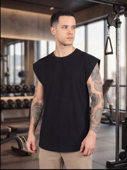 Man in black sleeveless gym shirt with tattoos, standing in fitness studio near weight equipment
