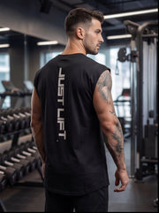 Man wearing black 'JUST LIFT' gym tank top, showcasing fitness apparel in a modern gym setting.