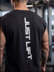 Man wearing black 'JUST LIFT' gym tank top, showcasing athletic build in fitness setting