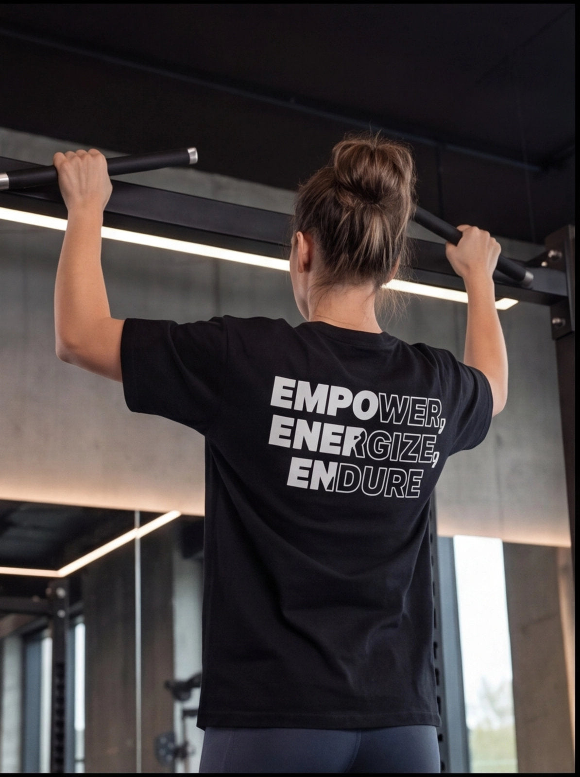 Woman doing pull-ups in gym wearing black 'EMPOWER, ENERGIZE, ENDURE' fitness t-shirt for functional training