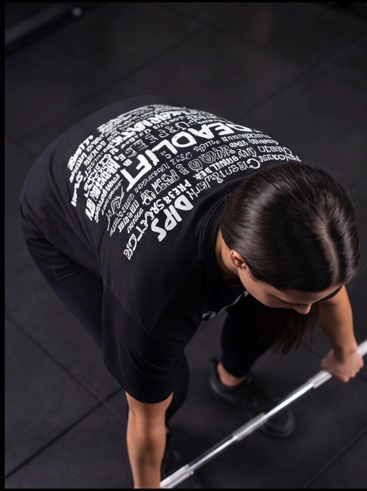 Woman in black fitness shirt performing deadlift with barbell in gym