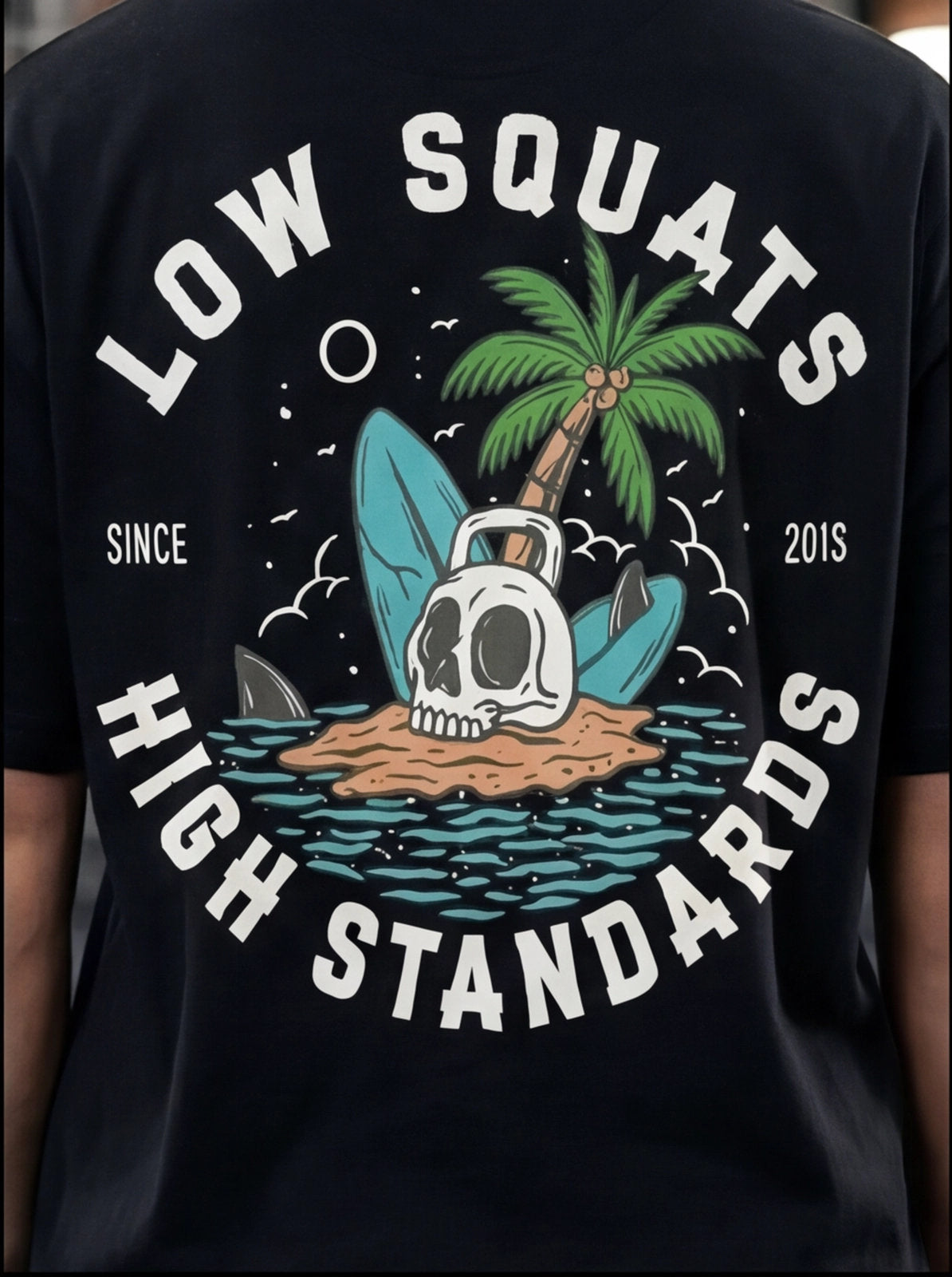 Black fitness tee with 'Low Squats High Standards' graphic, skull, palm tree, surfboard, kettlebell, since 2015