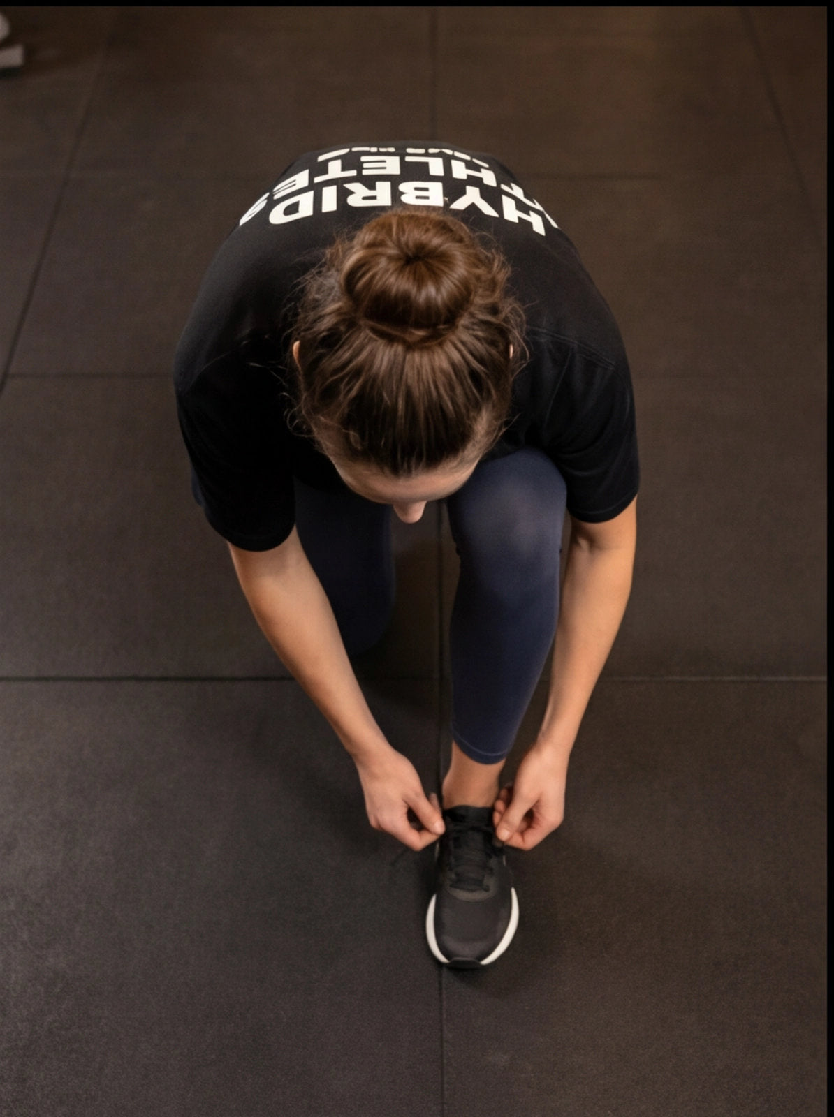 Athlete tying athletic shoes on gym floor, wearing Hybrid Athletes shirt for functional fitness training