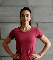 Female athlete in a pink fitness t-shirt standing confidently against a concrete wall