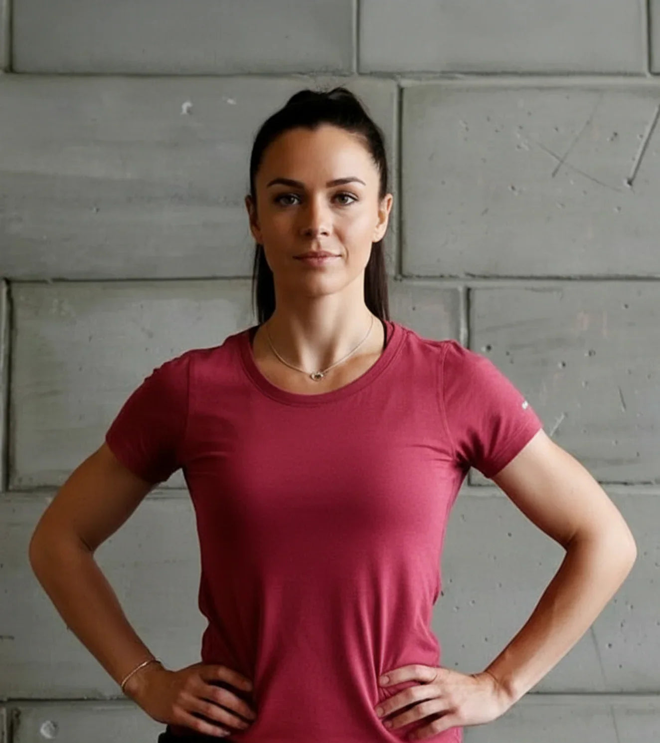 Female athlete in a pink fitness t-shirt standing confidently against a concrete wall