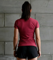 Woman in athletic maroon t-shirt and black shorts facing concrete wall, fitness apparel