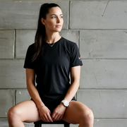Athletic woman in black performance t-shirt and shorts sits against concrete wall