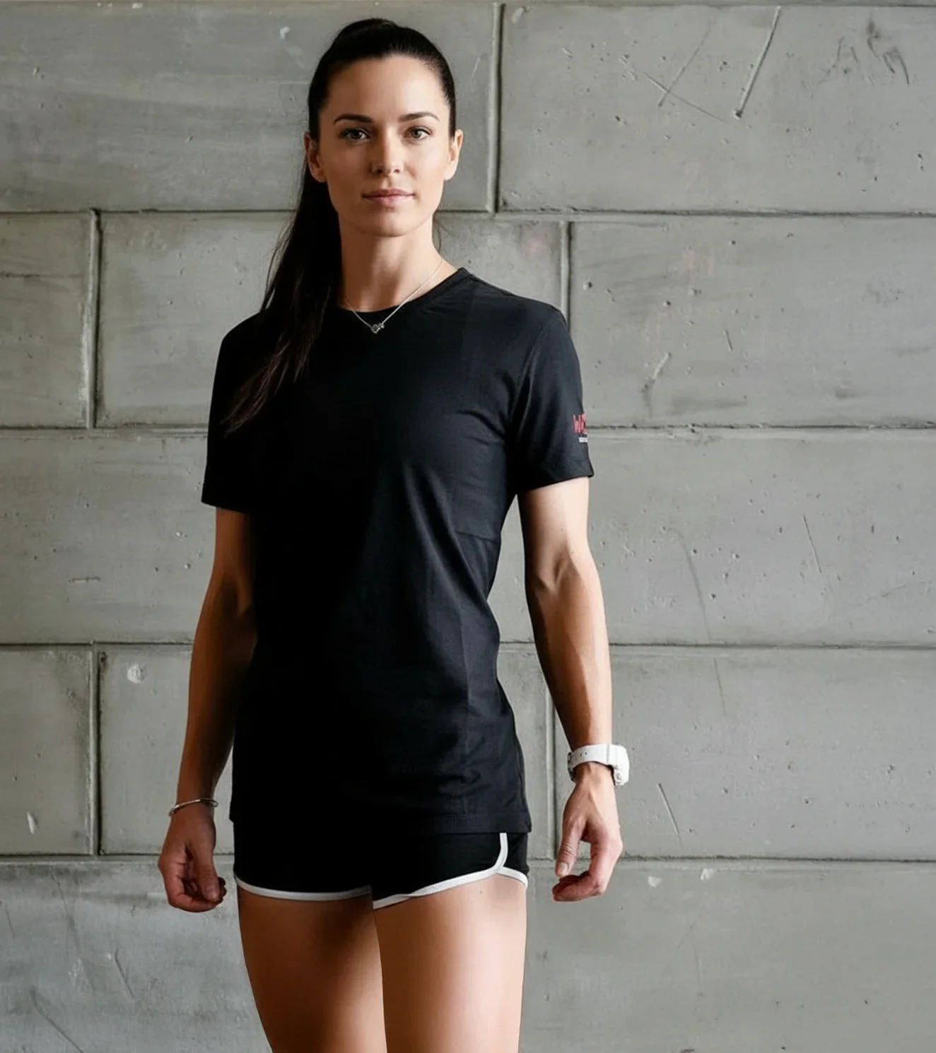 Woman in black athletic t-shirt and shorts standing against concrete wall, fitness apparel
