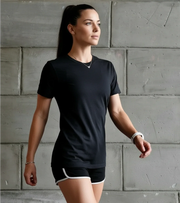 Woman in black athletic t-shirt and shorts standing against a concrete wall, fitness apparel