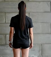 Female athlete in black workout shirt and shorts standing against a concrete wall