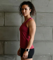 Athletic woman in red tank top and black shorts standing by a concrete wall, fitness watch on wrist