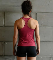 Woman in athletic burgundy tank top and black shorts facing gray gym wall