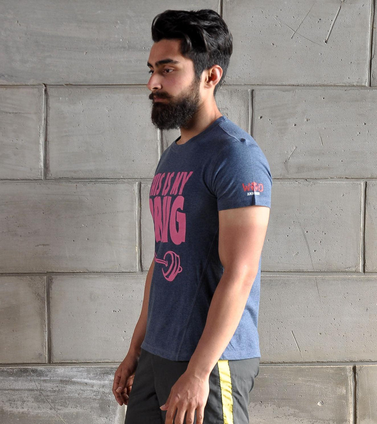 Man in a blue WOD Armour functional fitness t-shirt posing against a grey concrete wall.