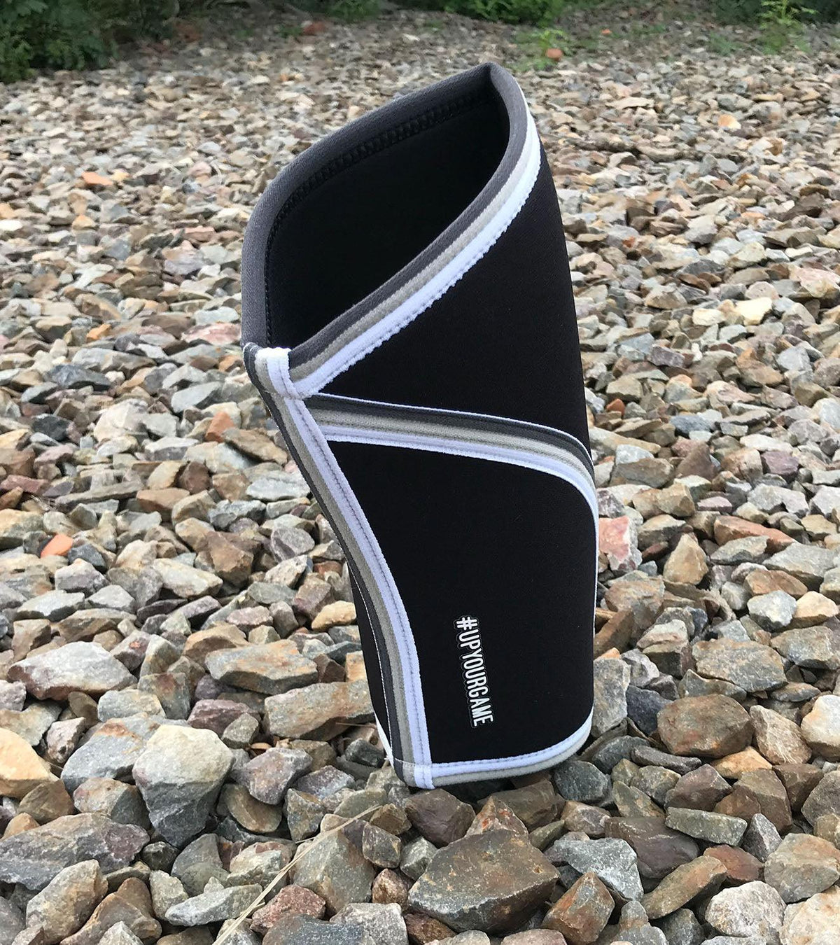 Black and white functional fitness elbow sleeve with #UPYOURGAME text on rocky ground