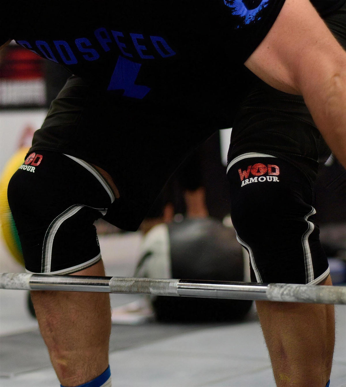 Close-up of an athlete wearing black WOD Armour knee sleeves while lifting a barbell.