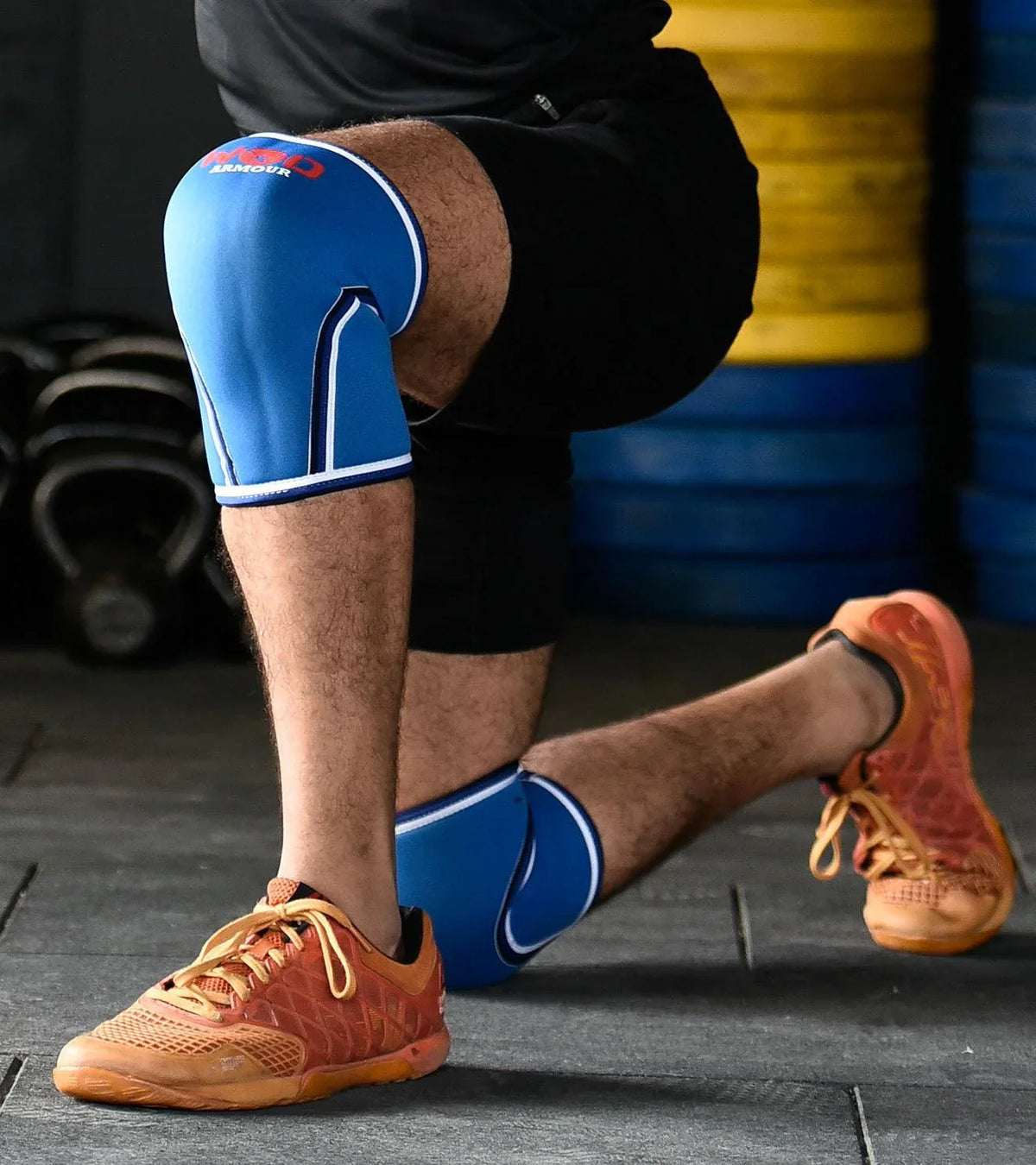 Athlete wearing blue supportive knee sleeves and orange training shoes during a workout.